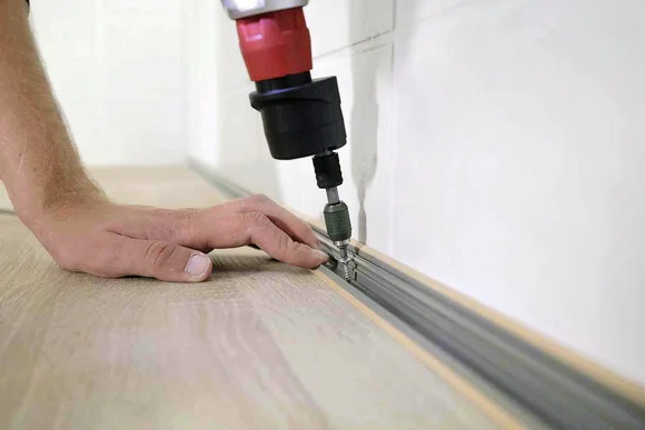 Person verschraubt eine Metallschiene auf dem Boden.